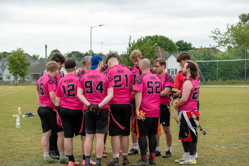 A flag american football team in pink jerseys huddling together